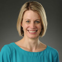 Dr. Christiana Zenner smiles in front of a dark background while wearing a blue shirt.